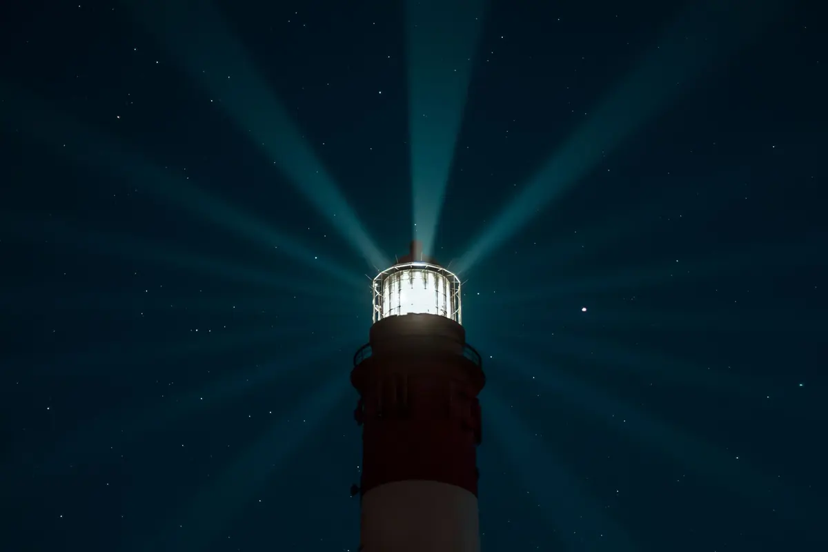 Leuchtturm bei Nacht, das Leuchtfeuer wirft Lichtstrahlen in den Sternenhimmel