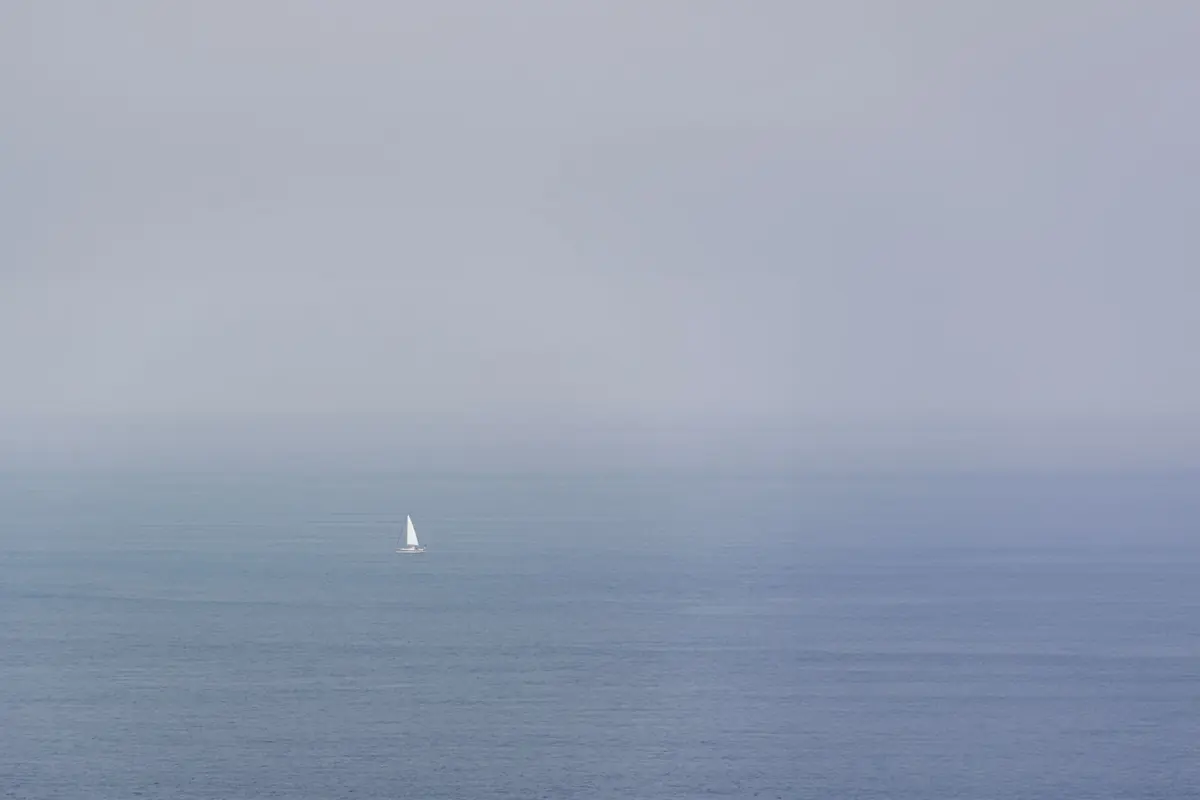 Ruhige See im Nebel, am Horizont ein einzelnes Segel