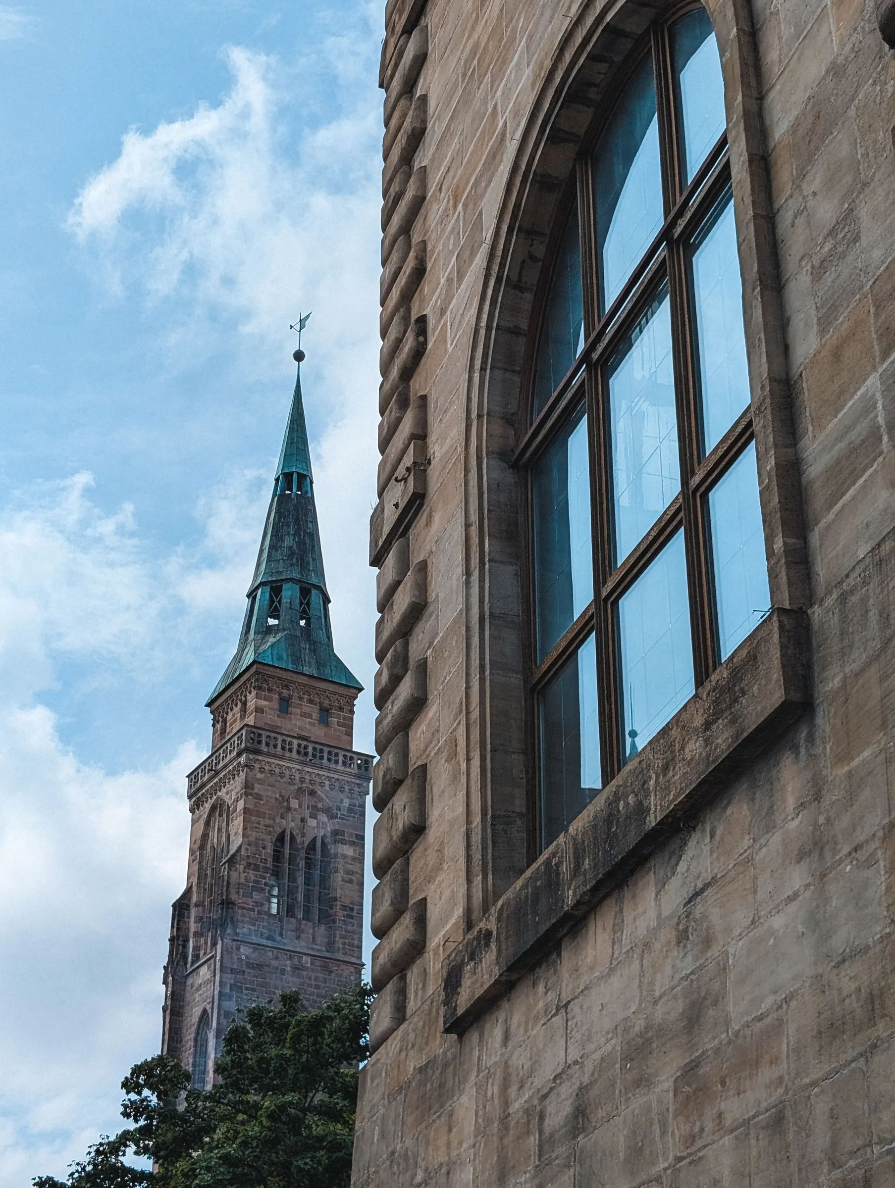 Sandsteinfassade mit Rundbogenfenster, dahinter ein gotischer Kirchturm in Nürnberg