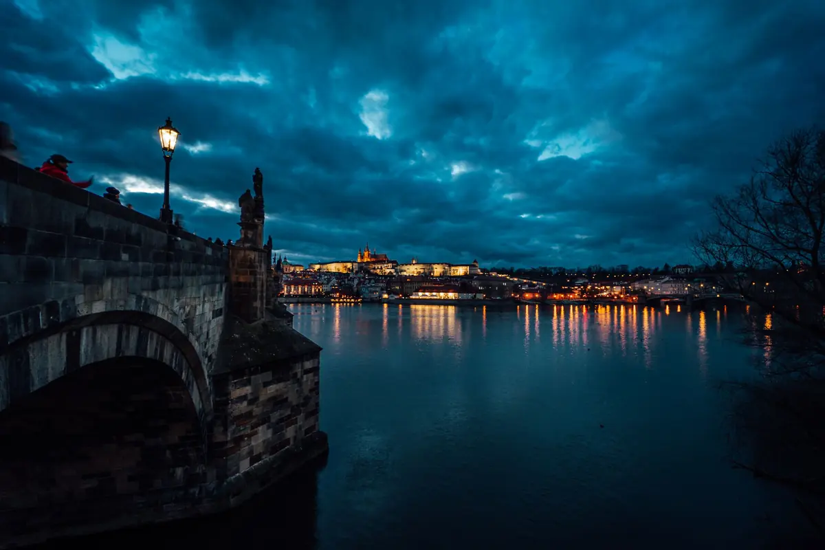 Karlsbrücke in Prag in der Dämmerung mit beleuchtetem Ufer