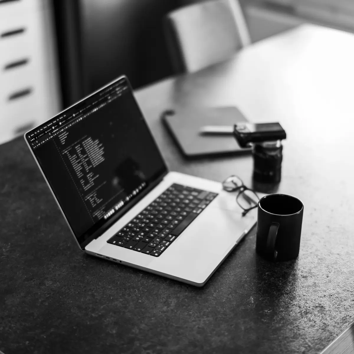 Aufgeklappter Laptop mit Quelltext auf einem Tisch, schwarz-weiß